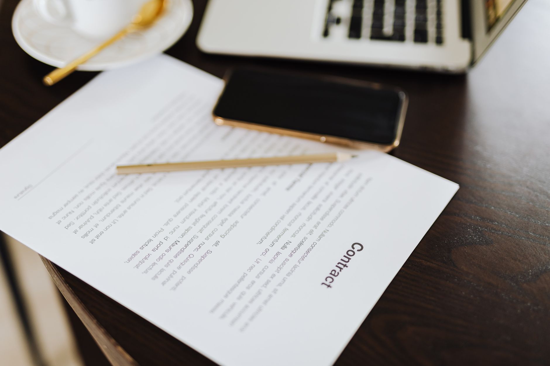 Gros plan d'un contrat avec des essentiels de bureau comme un ordinateur portable et du café sur un bureau.