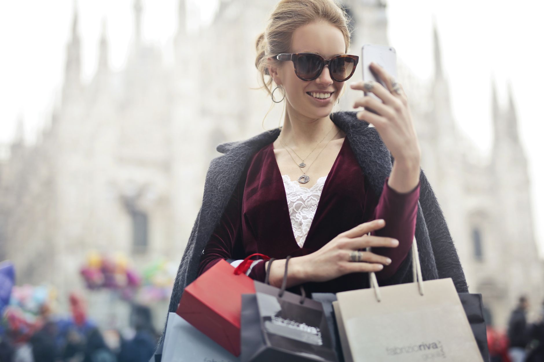 Femme élégante avec des sacs de shopping prend un selfie près du célèbre Duomo de Milan par une journée ensoleillée.